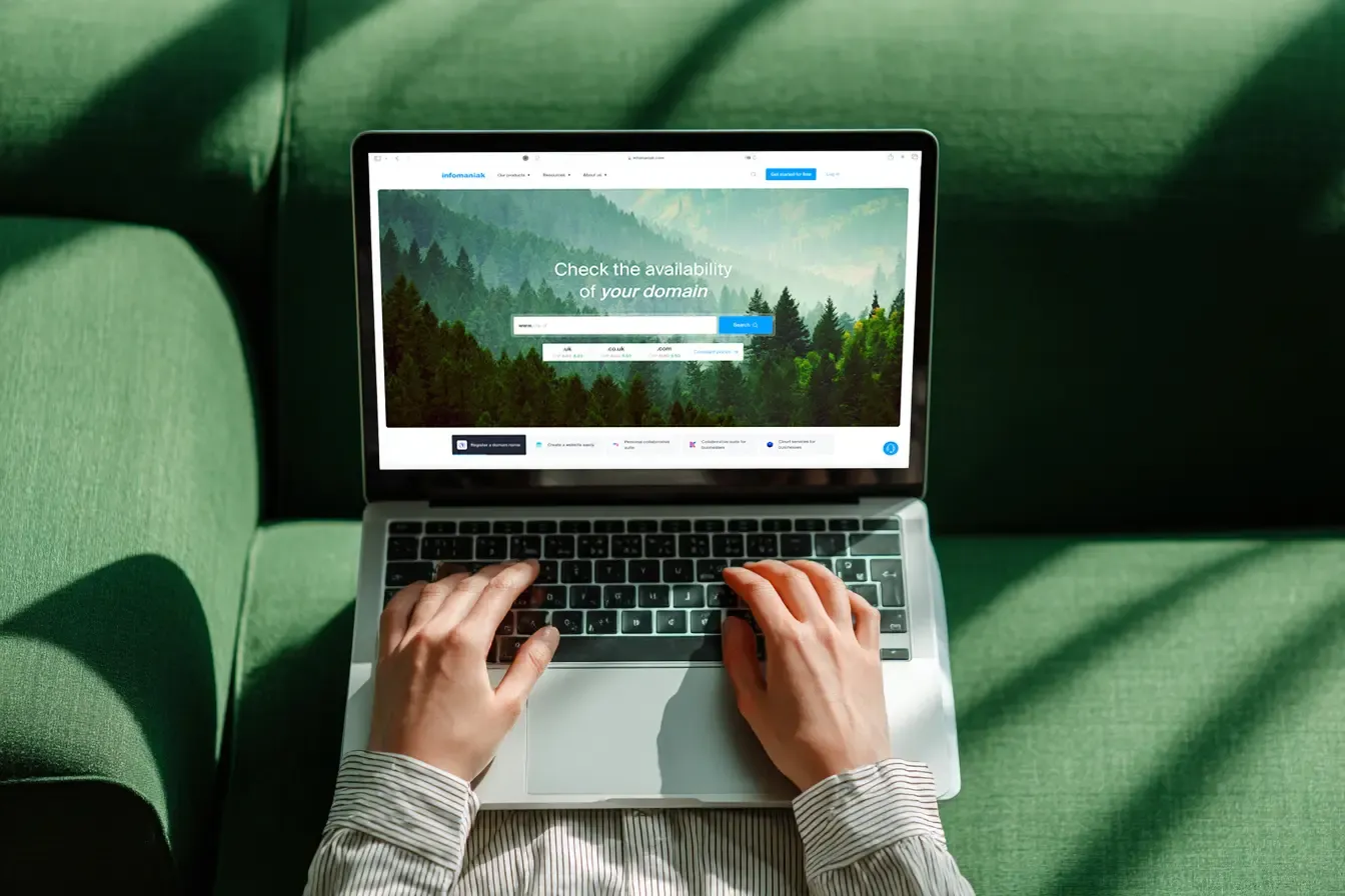 Top view of a person's hands typing on a laptop displaying the Infomaniak website